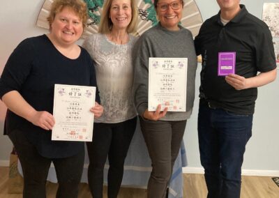 Four Shoden Reiki graduates holding certificates in front of a Japanese fan