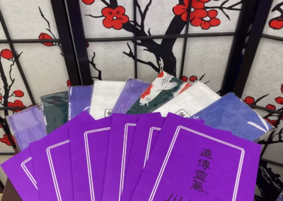 Purple Jikiden Reiki manuals fanned out in front of a Japanese cherry blossom screen