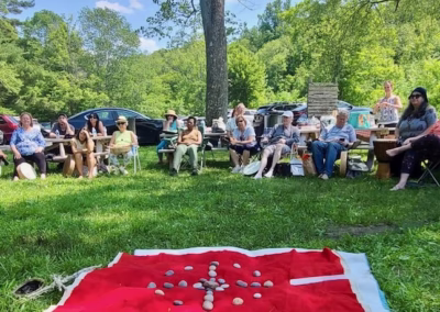 Group gathered outdoors around a medicine wheel blanket for a Summer Solstice ceremony
